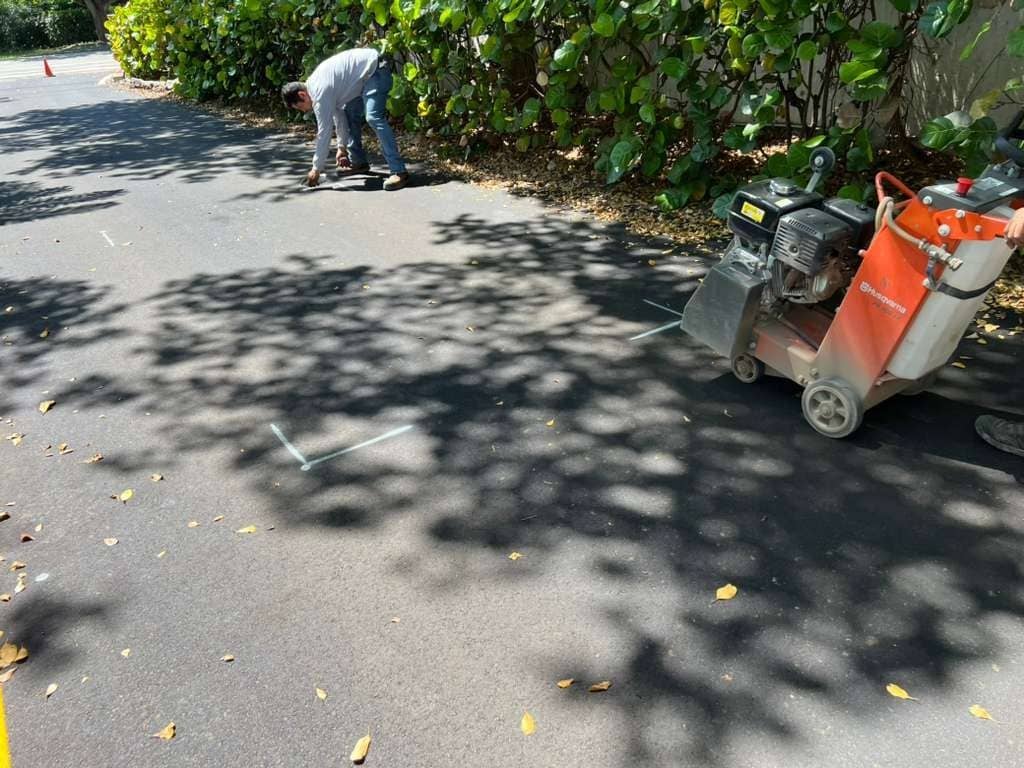 Technician marking a driveway for a saw-cut beside a concrete saw before the safety loop install